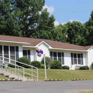 A suburban white house with a ramp, surrounded by trees.