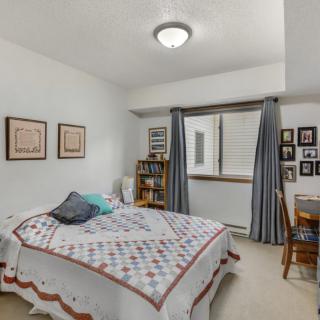 A cozy bedroom with a bed, wall artwork, a bookshelf, and a desk near the window.