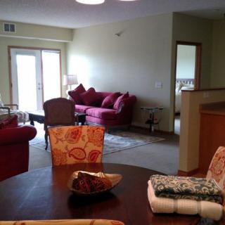 A cozy apartment living room with a dining area, featuring comfortable red sofas and a wooden dining table.