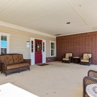 A cozy outdoor patio with a sofa and armchairs against a brick wall and a red front door.