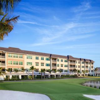 A luxurious resort building next to a manicured golf course under a bright blue sky.