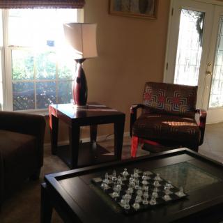 A cozy living room with a chess board on the table, surrounded by furniture and illuminated by natural light from a window.