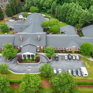 Aerial view of a large building surrounded by trees with a parking lot in front.