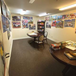 A cozy game room with tables, chairs, and various board games surrounded by colorful posters on the walls.