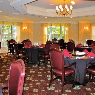 An elegant dining room with neatly arranged tables and chairs, featuring a chandelier and large windows.