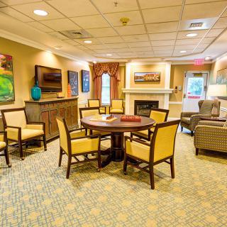 A cozy living room featuring a central round table, surrounding chairs, and warm interior decor.