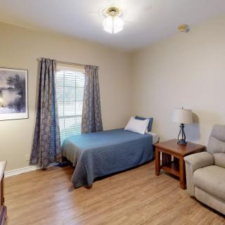 A cozy bedroom with a single bed, armchair, and wooden flooring.