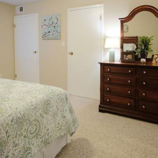 A cozy bedroom featuring a patterned bedspread, a dresser with a mirror, and decorative elements.