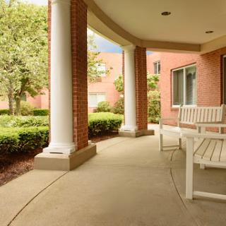A serene porch with a bench, surrounded by greenery and elegant columns.