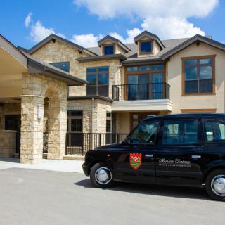 A luxury house with a stone facade and a black car parked in the driveway on a sunny day.