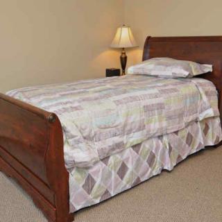 A neatly made bed with a wooden frame and a lamp on a bedside table.