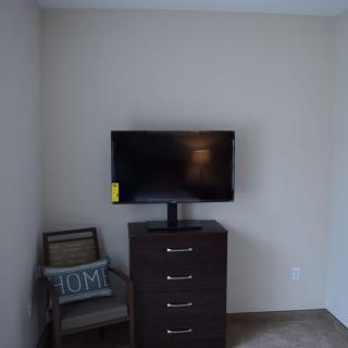 A minimalist room setup with a television on a dresser and a chair with a pillow.