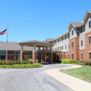 A modern building with a landscaped entrance and an American flag, set against a clear blue sky.