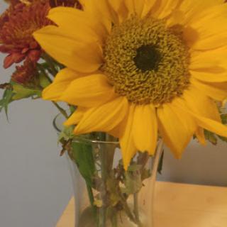 A vibrant sunflower surrounded by other colorful flowers in a glass vase.