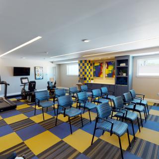 A multi-purpose room featuring arranged chairs, treadmills, and colorful artwork on the walls.