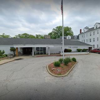 A facility entrance with a driveway and flagpole under a cloudy sky.
