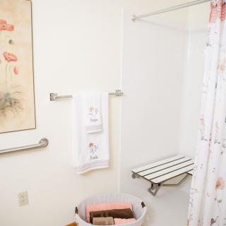A bathroom with a walk-in shower and seating bench, featuring a decorative towel and shower curtain.