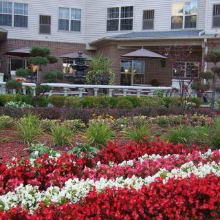 A beautifully landscaped garden with vibrant red and white flowers in front of a building with outdoor seating.