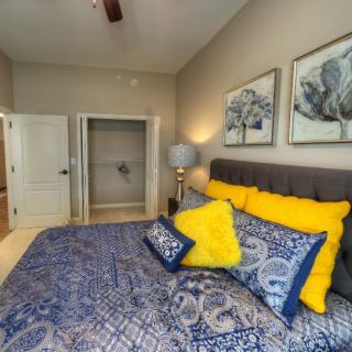 A modern bedroom featuring a bed with blue and yellow pillows, complemented by wall art and soft lighting.