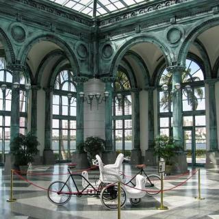 A historic indoor space featuring a bicycle carriage, with ornate arches and a glass ceiling.