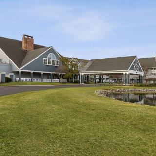 A picturesque building with a sloped roof surrounded by a well-maintained lawn and pond under a clear sky.