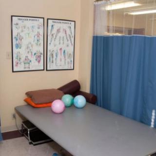 A physical therapy room with a massage table, exercise balls, and medical charts on the wall.