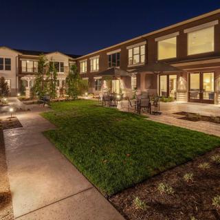 A beautifully lit mansion exterior at night, showcasing modern architecture and a well-maintained landscape.