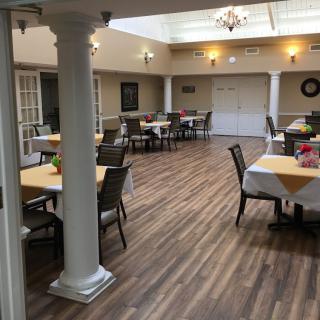 A spacious indoor dining area with neatly arranged tables and chairs, featuring wooden flooring and bright lighting.