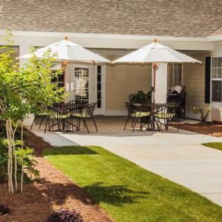 A tranquil patio area with tables and chairs shaded by umbrellas, surrounded by well-maintained landscaping.