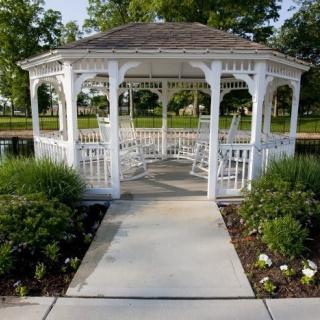 A white gazebo surrounded by greenery and a paved pathway in a garden setting.