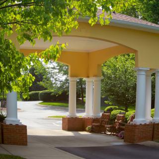An outdoor entrance with columns, featuring a landscaped driveway and surrounding greenery.