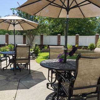 A sunny patio area with tables, chairs, and large umbrellas in a garden setting.