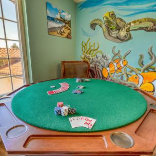 A game room featuring a poker table with playing cards and chips, surrounded by an underwater-themed mural.