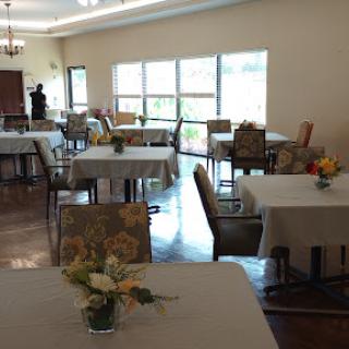 A spacious and well-lit dining area featuring neatly arranged tables and chairs, adorned with floral centerpieces.