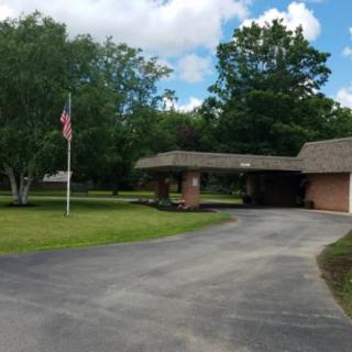 A house with a driveway and flagpole, surrounded by trees under a cloudy sky.