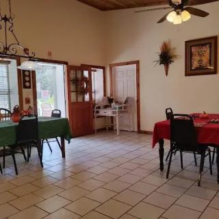 A cozy dining area featuring two tables set with colored tablecloths, surrounded by chairs and adorned with wall decorations.