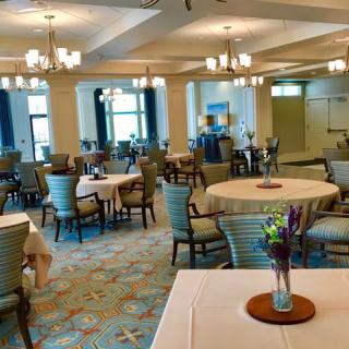 A spacious and elegantly decorated dining room with multiple tables and chairs, featuring floral centerpieces and warm lighting.