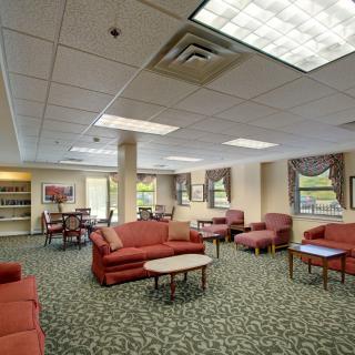 A spacious lounge area with sofas and chairs, adorned with carpet and lit by overhead lighting.