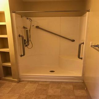 Accessible walk-in shower with grab bars and handheld showerhead.