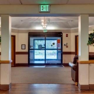 A well-lit hallway with an exit sign and double doors at the end, featuring decorative plants and seating.