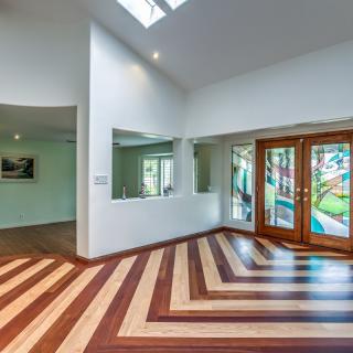A modern living room featuring a striking wooden floor pattern, large glass doors, and abundant natural light from a skylight.