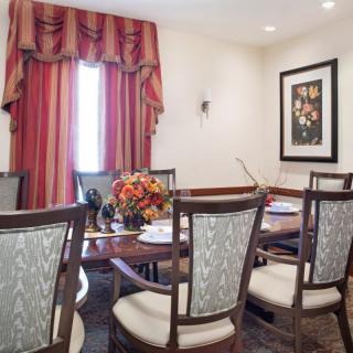 A cozy dining room with a wooden table, surrounded by upholstered chairs, adorned with red curtains and decorative items.