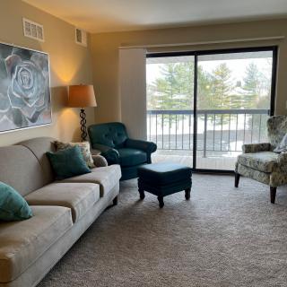 A cozy living room with a sofa, armchairs, and a large sliding door letting in natural light.