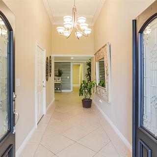 A welcoming entrance hallway with a chandelier, tiled floor, and decorative plants.