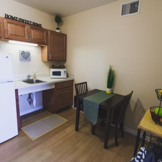 A compact kitchen and dining area featuring wooden cabinets, a small table with chairs, a microwave, and a sink.