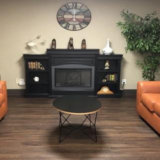 A cozy living room setup featuring a fireplace, two orange armchairs, a central coffee table, and decorative elements on the shelves.