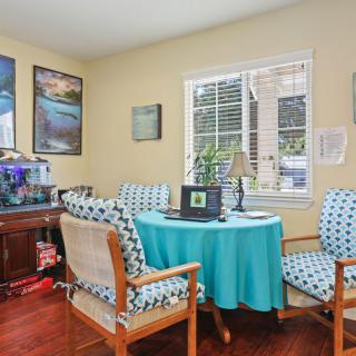 A cozy home office with a round table, patterned chairs, and an aquarium, featuring artwork on the walls.