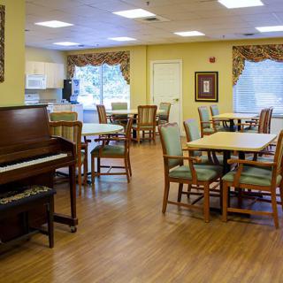 A cozy dining area with a piano, tables, and chairs on a wooden floor.