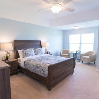 A cozy bedroom with a large bed, bedside tables with lamps, two chairs by the window, and bright natural lighting.