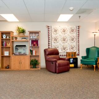 A cozy living room featuring an armchair, bookshelf, and decorative quilt on the wall.